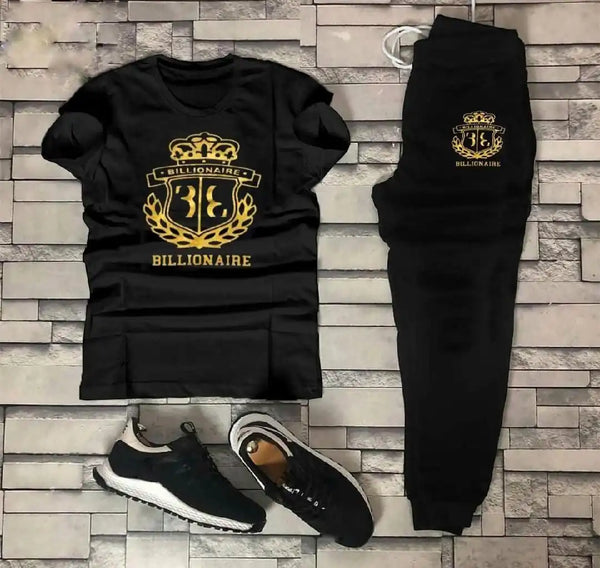 Black sweatshirt, black pants, and black sneakers with gold 'Billionaire' logo on a stone wall background.