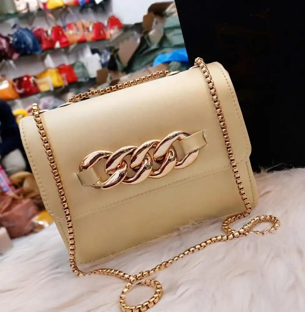 Beige handbag with gold chain detail on a white surface