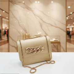 Beige handbag with gold chain detail on a white surface, blurred store interior in the background