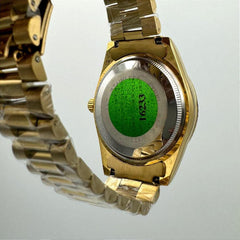 Gold watch with a green label on a light gray background